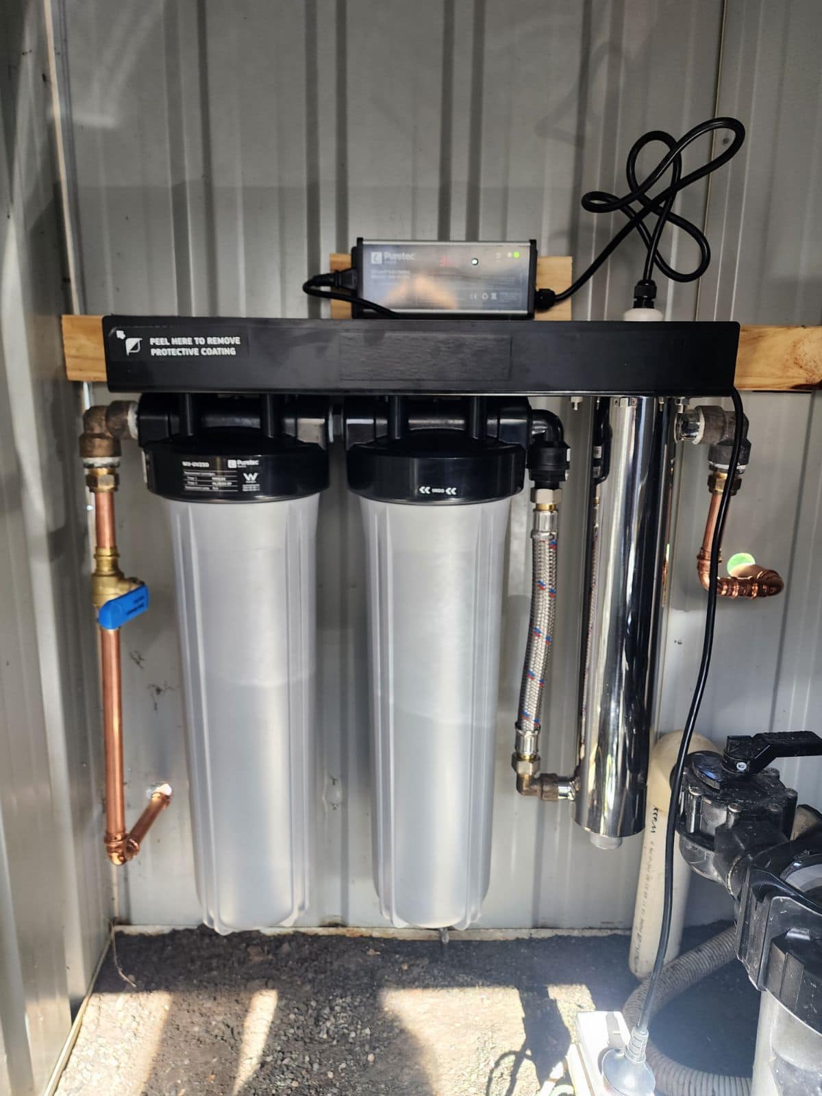 Whole-house water filtration system with UV steriliser mounted on a wall