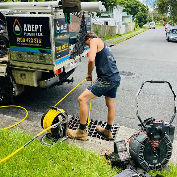 Adept Plumbing & Gas plumber clearing a blocked stormwater drain with a jetting hose beside the branded service ute