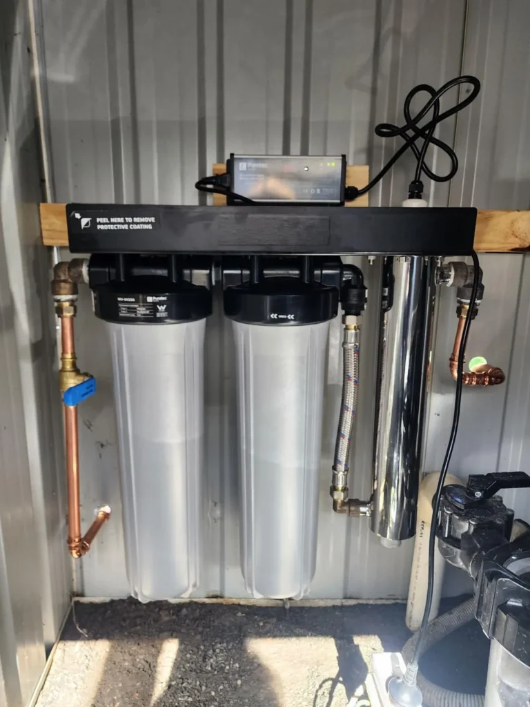 Whole-house water filtration system with UV steriliser mounted on a wall