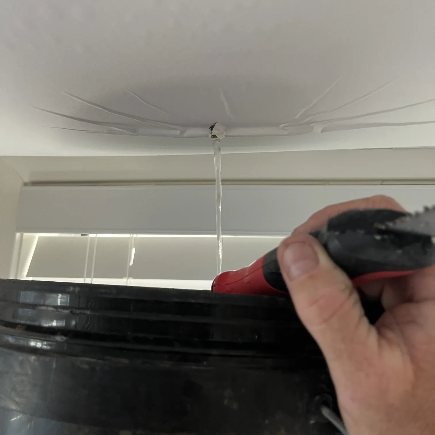 Water leak coming through a ceiling with a stream of water caught in a black bucket, highlighting the need for professional water leak detection and repair services.
