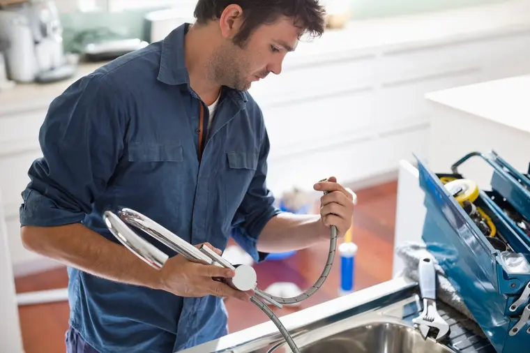 Plumber fitting a flexible hose to a new kitchen mixer tap beside a stainless steel sink