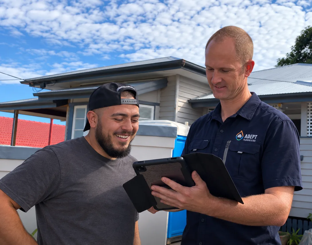 Two Adept Plumbing & Gas team members going through a job on a tablet outside a home
