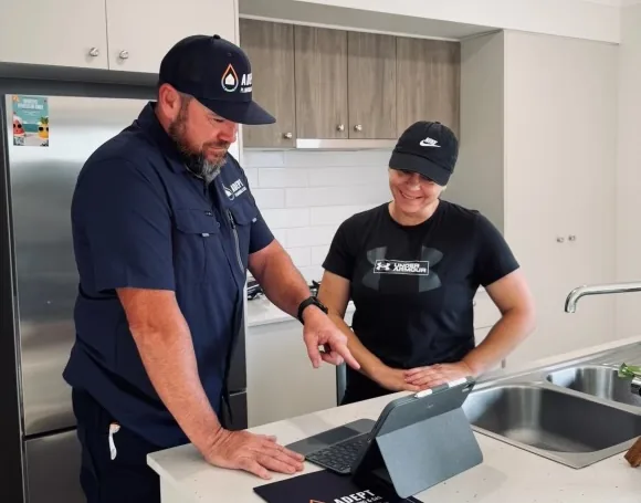 Two Adept Plumbing & Gas team members reviewing a job on a tablet in a kitchen