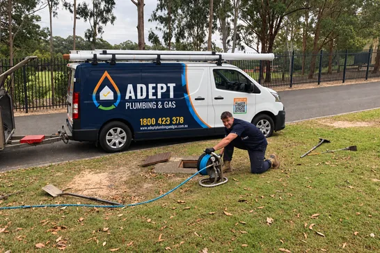 Plumber clearing a blocked drain on a front lawn beside an Adept Plumbing & Gas van
