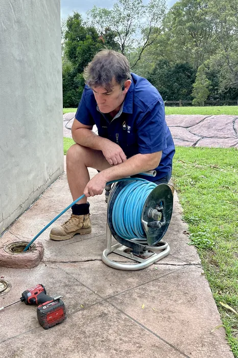 Plumber clearing an outdoor drain with a hose reel drain jetter