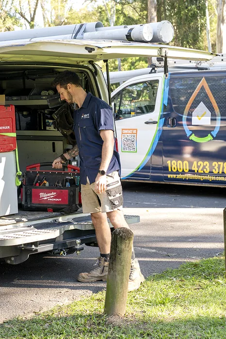 Adept Plumbing & Gas technician loading equipment into a branded service van