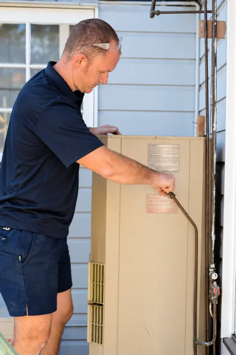 Plumber working on a gas hot water unit mounted outside a home