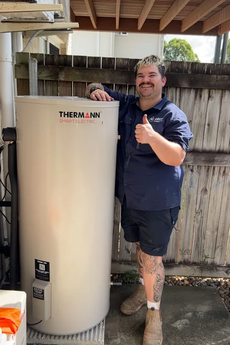 Plumber beside a newly installed electric hot water system