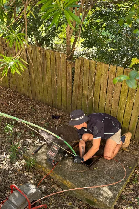 Plumber working at a drain access point in a backyard