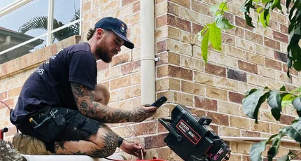Plumber working at a downpipe beside a brick home in Logan