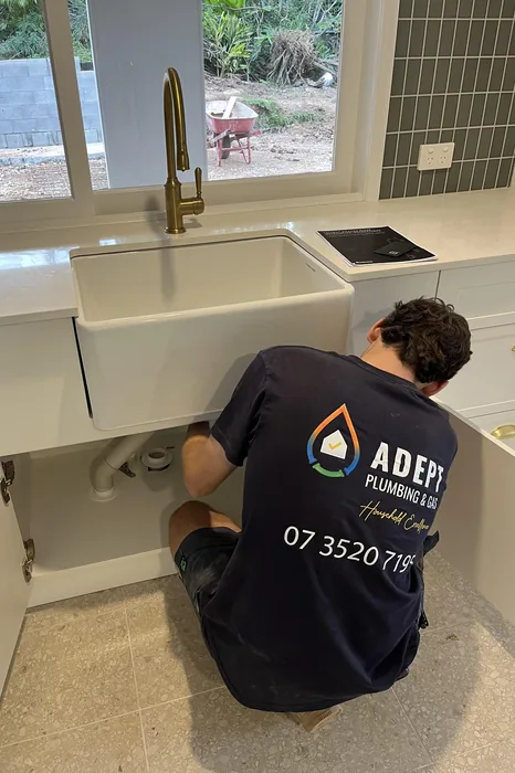 Adept Plumbing & Gas plumber testing pipework under a kitchen cabinet in Logan