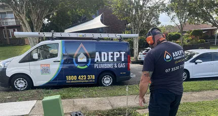 Adept Plumbing & Gas plumber locating a line on a front lawn in Logan, with the company van behind