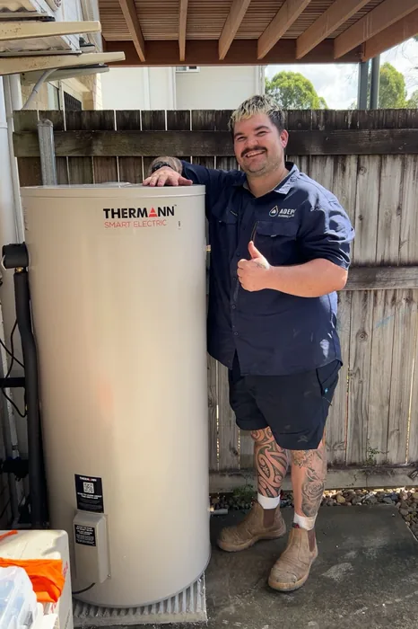 Adept Plumbing & Gas plumber beside a newly installed Thermann electric hot water system in Shailer Park