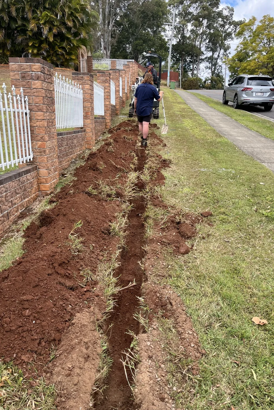 Adept Plumbing & Gas plumber laying new pipework along a fence line in Tanah Merah