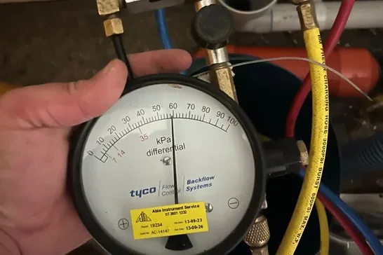 Plumber reading a backflow test gauge during an annual device test