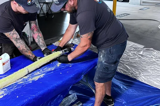 Two plumbers preparing a pipe relining liner in a basement car park