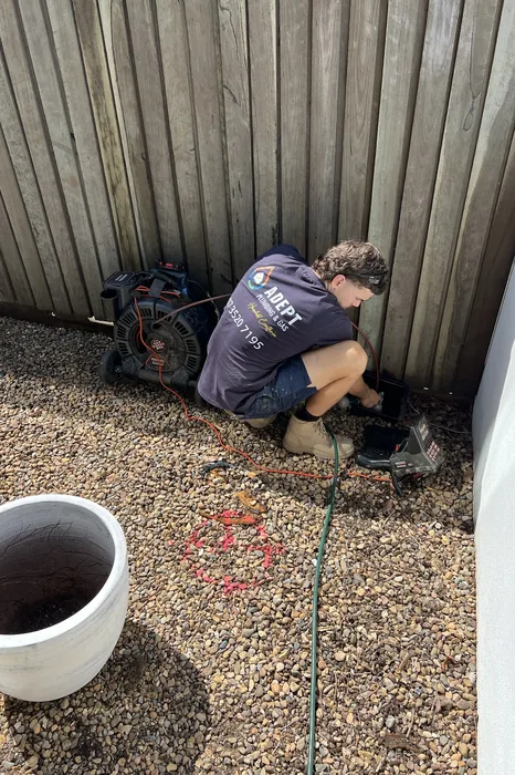 Plumber clearing a blocked drain beside a fence in Kingston