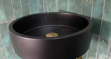 Black round basin with brass tapware against green tiles in Logan