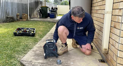 Plumber using an electronic leak locator beside a home in Waterford