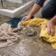 Homeowner placing towels around an overflowing drain while waiting for emergency blocked drain plumber
